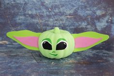 a green and pink stuffed animal with big ears on it's head, sitting on a wooden surface