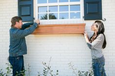 a man and woman standing next to each other in front of a white brick building