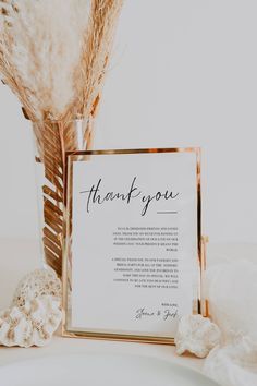 a thank you card sitting on top of a table next to a vase with feathers