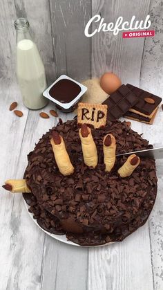 a cake with chocolate frosting and hot dogs on it, surrounded by ingredients for the recipe