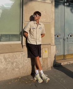 a man leaning against a wall with his hands on his hips wearing sunglasses and shorts