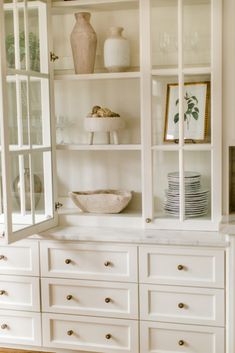 a white china cabinet filled with dishes and vases