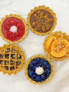 four pies with different toppings are arranged on a white tablecloth and one has fruit in the middle