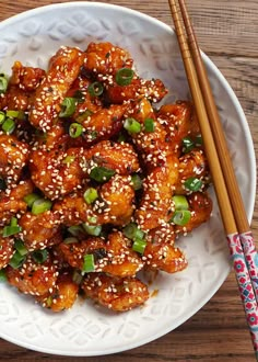 a white plate topped with chicken covered in sesame seeds and green onions next to chopsticks