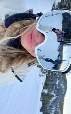 a woman wearing ski goggles standing in the snow with her reflection in the sunglasses