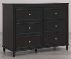 a black dresser with gold knobs on the top and bottom drawers, against a white wall