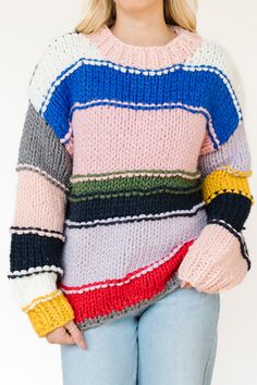 This sweater is a striking example of a chunky, hand-knit garment featuring a patchwork-like design with bold, contrasting colors. The sweater is made from thick yarns, creating a warm and cozy feel that is ideal for colder weather. It has a high, slightly ribbed neckline, which adds to the snug, comfortable look of the piece.

The design is characterized by wide, horizontal stripes in a variety of colors, including pastel pink, deep blue, lavender, mustard yellow, forest green, and bold red.