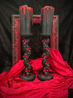 two black candles with red drips on them sitting in front of a dark background