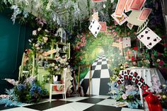 a room filled with lots of flowers and cards hanging from the ceiling next to a checkered floor