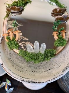 a mirror with moss and rocks in the middle on a wooden table next to other glass objects