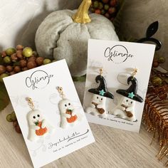 two halloween themed earrings are on display next to some pumpkins and other holiday decorations