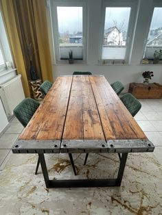 a large wooden table sitting in front of two green chairs on top of a rug