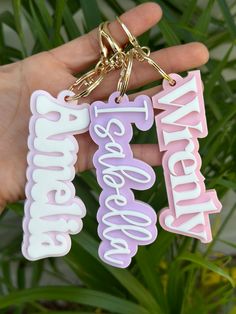 someone is holding two key chains with the words awesome and wonderful on them in front of some plants