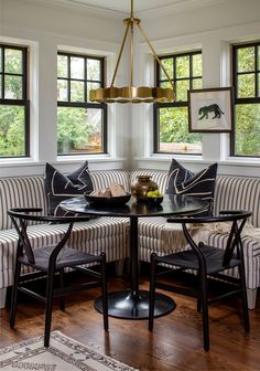 a dining room table with four chairs and a bench in front of two large windows