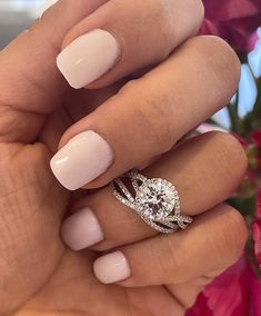 a woman's hand holding a ring with a diamond on it and pink flowers in the background