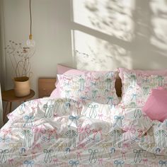 an unmade bed with pink and blue bows on the comforter, next to a potted plant