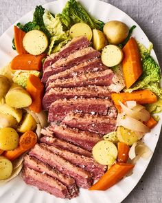 a white plate topped with meat and veggies on top of a table next to potatoes