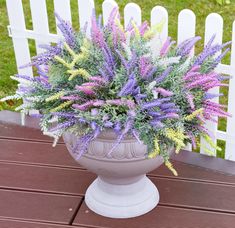 a potted plant with purple and yellow flowers sitting on a wooden table next to a white picket fence