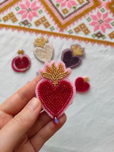 a hand holding a small heart shaped brooch in front of some other pins and sequins