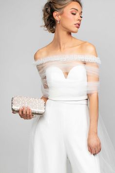 a woman in white is holding a purse and wearing a wedding dress with sheer sleeves