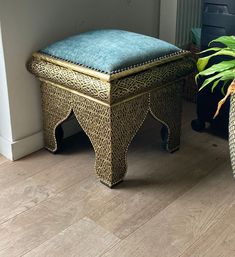 a blue ottoman sitting on top of a wooden floor next to a potted plant