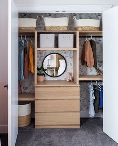 an open closet with clothes hanging on the wall and a round mirror in the middle