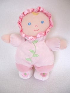 a small doll with pink clothes and a flower on it's head, sitting on a white surface