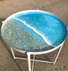 a blue table with sand and water in it sitting on the ground next to an ocean wave