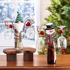 three wine glasses with snowmen in them sitting on a table next to a christmas tree