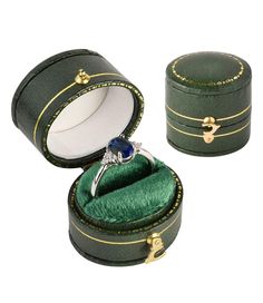 an open green velvet ring box with a blue stone in the center and gold trimmings