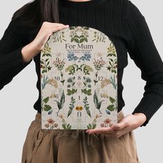 a woman holding up a book with floral designs on the front and back cover that reads for mum