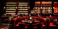 a dimly lit restaurant with red velvet booths and tables in front of bookshelves