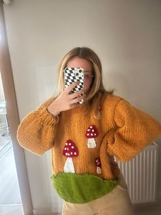 a woman taking a selfie in front of a mirror wearing an orange sweater with mushrooms on it