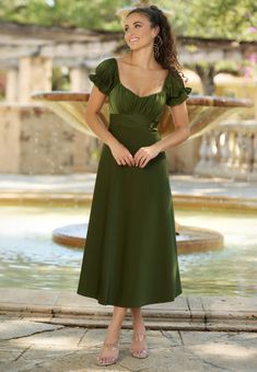 a woman standing in front of a fountain wearing a green dress with puffy sleeves