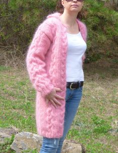 a woman standing in the grass wearing a pink cardigan sweater and jeans with her hands on her hips