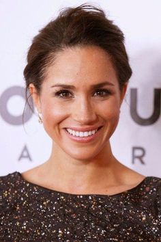 a smiling woman in a black and gold dress with her hair up into a bun