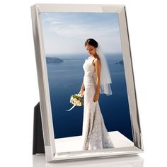 a woman in a wedding dress standing next to a window with the ocean behind her