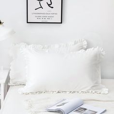 a white bed with two pillows and a magazine on the headboard next to it