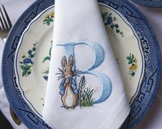 a napkin with the letter b on it and a bunny holding flowers is sitting on a plate