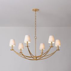 a gold chandelier with white shades hanging from it's center beam in a living room