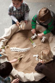 three children are playing with sand and plastic animals