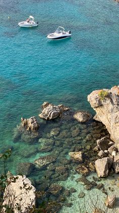 three boats floating on top of a body of water next to rocky shore covered in green algae