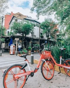 two orange bikes parked next to each other on the side of a road in front of a building