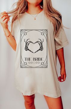 "This boho celestial bachelorette party shirt will be a crowd favorite! It features a beautiful design of a tarot love bride and spooky skeleton rock party. With a designation of either \"The Bride\" or \"The Party\" you can celebrate in style, with wine, tarot cards, astrology, magic and mischief. Perfect for any bachelorette party! White & Natural: \"The Bride\" Black & Peach: \"The Party\" We use the best material for extremely soft and comfortable wear. All of our shirts are printed so the i Bohemian Short Sleeve Tops For Wedding, Celestial Bachelorette Party, Celestial Bachelorette, Astrology Magic, Boho Celestial, Bachelorette Party Shirt, Black Peach, Group Shirts, Bohemian Bride