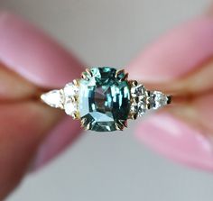 a woman's hand holding an emerald and diamond ring