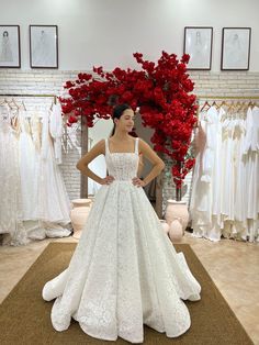 a woman standing in front of a wedding dress with red flowers on the wall behind her