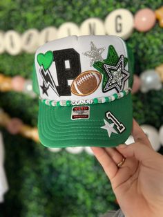 a person holding up a green and white baseball cap with the word p on it