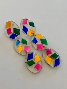 three pairs of multicolored earrings on a white surface with one earring missing