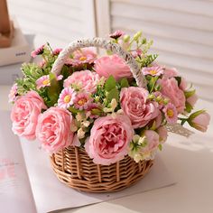 a basket filled with pink flowers sitting on top of a table next to an open book