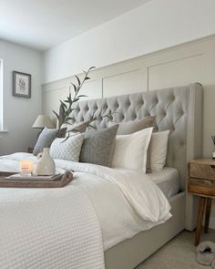 a bed with white linens and pillows in a bedroom next to a wooden table